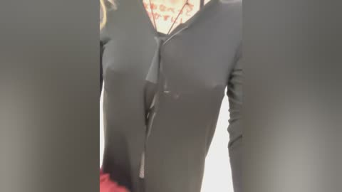 A video capturing the lower half of a person's torso, featuring grey pants and a glimpse of a white shirt with red text, likely in a public restroom.