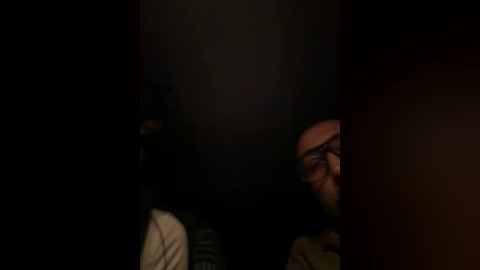A dimly-lit video featuring a man with glasses, partially obscured by shadow, and a dark, indistinct background. The image has a moody, mysterious atmosphere.