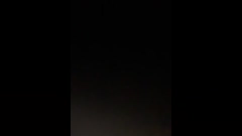 A dimly lit video with a black background, featuring an indistinct, shadowy figure in the center, possibly human, creating a mysterious and eerie atmosphere.