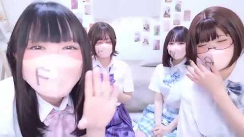 A video of four young Japanese girls in school uniforms, smiling and blowing kisses, in a brightly lit bathroom with a white toilet and a collage of photos on the wall.