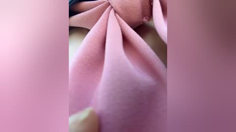 Close-up video of a soft, pink, textured fabric, possibly silk, with a folded-over edge, showing subtle creases and a smooth, shiny surface. The background is blurred, focusing attention on the fabric's delicate texture.