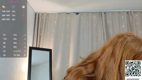 Video of a woman with long, wavy brown hair, seen from behind, in a room with beige curtains and a mirror. A QR code is visible in the bottom right corner.