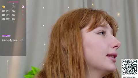 Video of a fair-skinned, red-haired woman with long bangs, wearing a green shirt, captured in a virtual reality setting. Background shows a blurred, semi-transparent VR headset display.