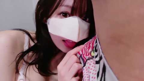 A video featuring an Asian woman with long black hair and light skin, wearing a white surgical mask, seductively biting into a red and white striped tie, suggesting an erotic context.