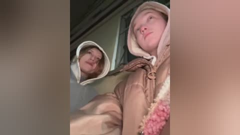 Video of a young woman in a beige fur hooded coat, with a pink scarf, standing in front of a mirror, capturing her reflection.