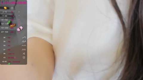 A close-up video of a woman's upper body in a white sweater, focusing on her chest. The background shows a smartphone screen with a chat app interface, displaying text and emojis.