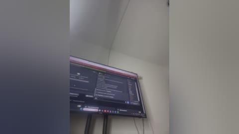 A video of a corner of a room featuring a large, flat-screen television mounted on the wall, displaying a black screen with white text. The wall is light-colored, and the room appears dimly lit, with a slightly blurred background.