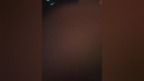 A close-up video of a nude woman's lower abdomen and thighs, showcasing smooth, fair skin with a subtle shine, set against a dimly lit, reddish-brown background.