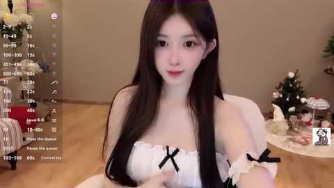 Video of an East Asian woman with long black hair, fair skin, and a slender build, wearing a black and white maid outfit, seated in a cozy room with a Christmas tree and a fireplace in the background.