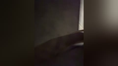 A dimly lit video of a person's hand, possibly female, with delicate fingers, partially obscured by shadow and a soft, diffuse light source. The background is a dark, indistinct blur, focusing on the subtle textures of the hand.