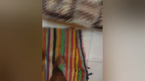 A blurred video of a person wearing a vibrant, multi-colored striped poncho with a white background, standing in a dimly lit room. The image is out of focus, making it difficult to discern details.