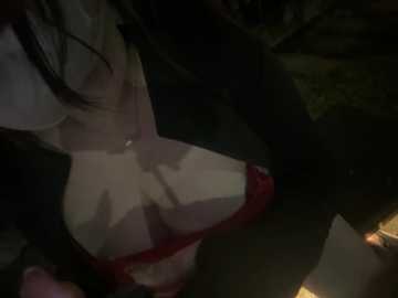 Video of a close-up of a woman's chest, wearing a black jacket and a red bra, with a dark, shadowy background.