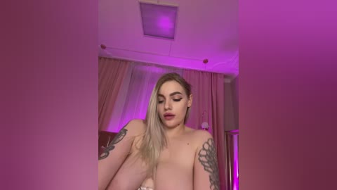 Video of a topless, fair-skinned woman with blonde hair, tattoos on her arms, and full lips, standing in a room with pink curtains and purple lighting.