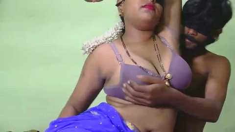 Video of a dark-skinned woman in a purple bra and blue skirt, with a dark-skinned man embracing her from behind.