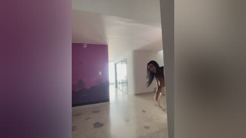 A video of a woman with long dark hair, naked, running into a room with a large, colorful mural on one wall and a polished marble floor.