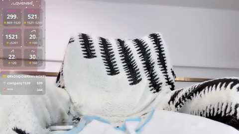 Video of a person's chest covered by a black-and-white striped blanket in a white room, with a digital display overlay showing health vitals like temperature, heart rate, and oxygen levels.