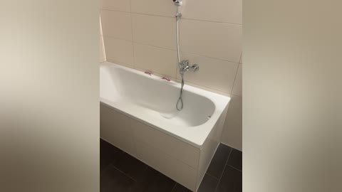 A video of a modern bathroom with a white bathtub, silver showerhead, and beige tiled walls. The floor is covered with dark tiles, and the space is clean and minimalist.