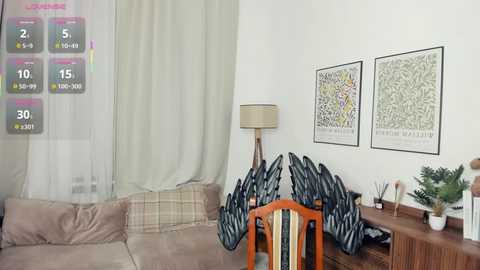 Video of a cozy living room with beige sofa, wooden chair, green curtains, white wall, framed botanical prints, and a tall floor lamp.
