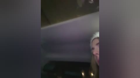 A blurry video of a partially obscured person with a white headband, likely female, smiling, taken indoors with dim lighting.