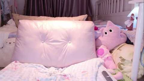 Video of a cozy bedroom with a white, tufted pillow and a pink, plush animal toy on a bed with light-colored, floral-patterned sheets.