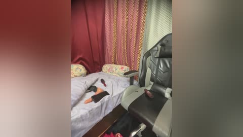 Video of a modestly furnished room with a bed, chairs, and a red curtain; a woman lies on the bed, wearing a black top, and a child is seated nearby.