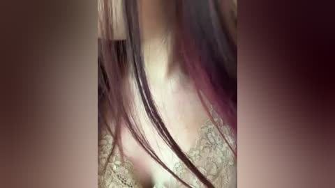 Close-up video of a woman's bare chest, featuring long, dark brown hair with purple highlights, cascading over intricate, lace-trimmed lingerie. The background is blurred, focusing on the hair and lace texture.