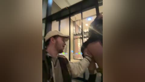 A video captures a man wearing a beige cap and jacket, restraining a woman with dark hair, inside a dimly lit, cluttered room.