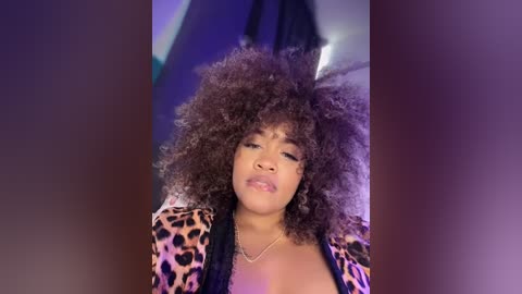 Video of a young African-American woman with voluminous, curly hair and a leopard-print jacket, smiling seductively, indoors with blurred background.