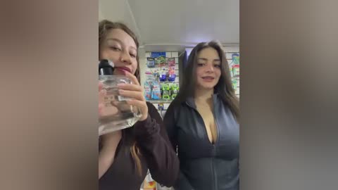 Video of two women in a convenience store, one holding a clear bottle, the other smiling in a black jacket. Background features colorful shelves of snacks.