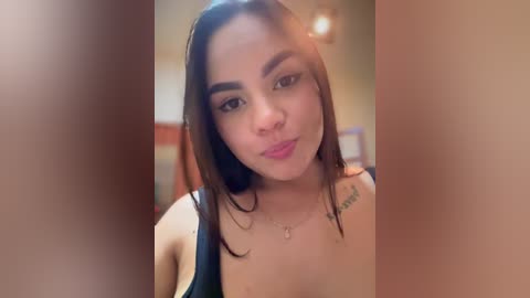 A video of a Latina woman with medium skin tone, long dark hair, and a tattoo on her right shoulder, wearing a black tank top, making a pouty face.