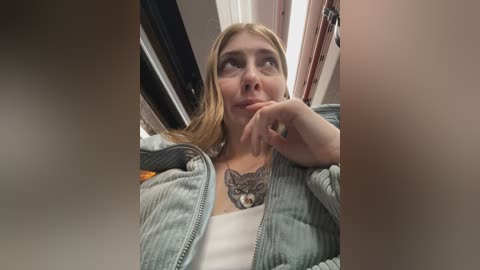 A video shows a blonde woman with a tattoo of a wolf on her chest, wearing a gray jacket, looking thoughtful.