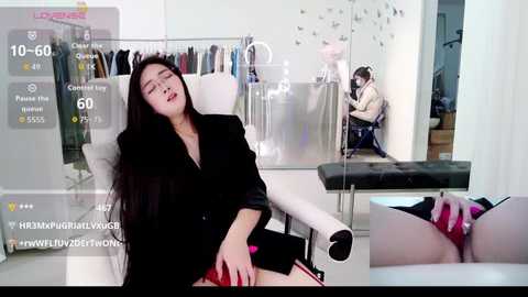 Video of an Asian woman with long black hair, wearing a black blazer and skirt, lying on a white examination table, eyes closed, in a clinical setting.