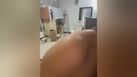 Video of a dimly lit room with a woman's bare buttocks in the foreground, surrounded by cardboard boxes, clothes, and a bed in the background.