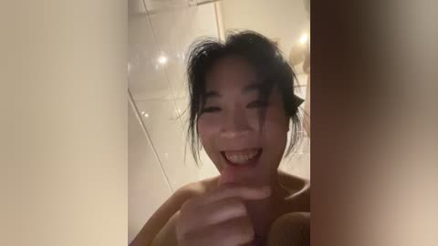 A candid video of a smiling Asian woman with dark hair, wearing a yellow top, captured from a low angle, emphasizing her playful expression.