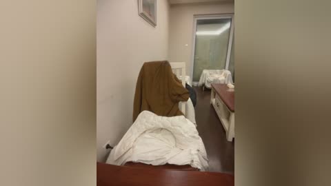 Video of a hospital room with a brown blanket draped over a bed, white sheets, a bedside table, and a door leading to another room.