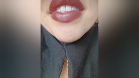 A close-up video of a person's lips and upper chest, showing light skin, full lips painted in deep red lipstick, and a black leather jacket with a golden zipper. The background is blurred, focusing attention on the subject.