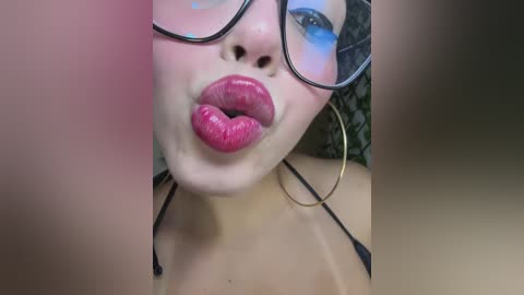 Video of a close-up of a woman's face with large, round glasses, bold pink lipstick, and hoop earrings. She's wearing a black bralette.