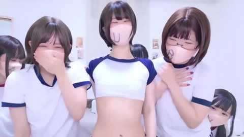 Video of three young Asian women with short hair, wearing white sports shirts with blue trim, and surgical masks, smiling and covering their mouths, indoors.