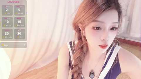 Video of an Asian woman with long, light brown hair styled in a braid, wearing a sleeveless, navy blue dress, standing in a softly lit room with wooden floors.