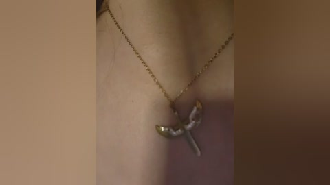 Video of a close-up of a person's neck, showcasing a delicate gold chain necklace with a small, ornate crucifix pendant. The background is blurred, with a warm, brownish hue.