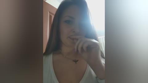 A video of a young woman with long brown hair, fair skin, and a small tattoo on her chest, posing in a dimly lit hallway, partially obscured by door frames.