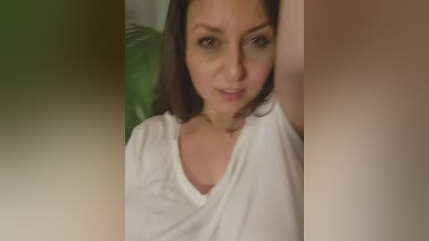 Video of a woman with medium skin tone and brown hair, wearing a white t-shirt, looking slightly to the side with a neutral expression.