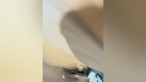 A blurry video of a person with light skin tone, wearing a dark outfit, bending down, possibly picking up an object. The background is indistinct, suggesting an indoor setting with muted colors.