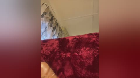 A video showing a partially blurred room with a red, plush blanket, a beige curtain, and a textured, beige wall. The image has a soft focus and a warm, muted color palette.