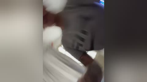 A blurry video shows a person with light skin, wearing a white shirt, holding a white object, possibly a bottle or a piece of paper. The background is out of focus.