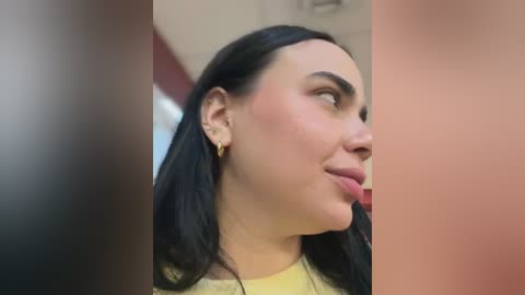 A video featuring a close-up side profile of a woman with long, straight black hair, fair skin, and subtle makeup. She has a confident expression, wearing a yellow top and small gold earrings.