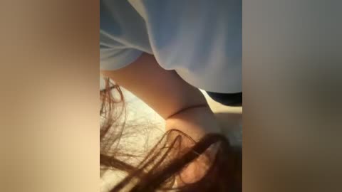 A close-up video showing a person's legs and torso, with light skin and brown hair, wearing light blue clothing, in a dimly lit room.