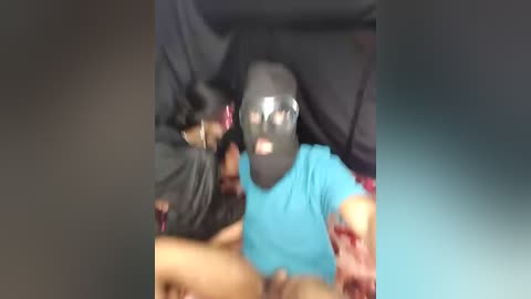 Video of a young man in a black balaclava and blue shirt, surrounded by people in dark clothing, possibly during a protest or unrest.