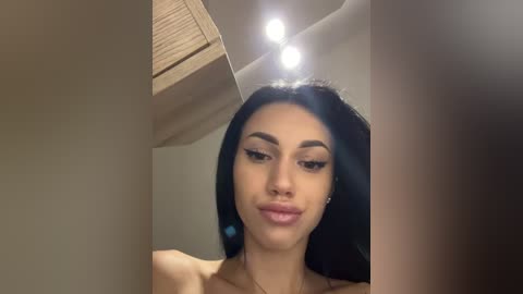 Video of a young woman with long black hair and light brown skin, wearing black eyeliner and nude lipstick, captured indoors under soft lighting.