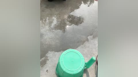 Video of a turquoise plastic bucket on a cracked, gray concrete surface, with a person's shadow partially visible, suggesting a sunny day.